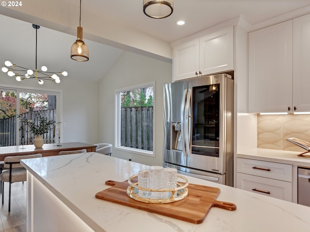 kitchen featuring light stone countertops, white cabinetry, plenty of natural light, backsplash, and stainless steel fridge