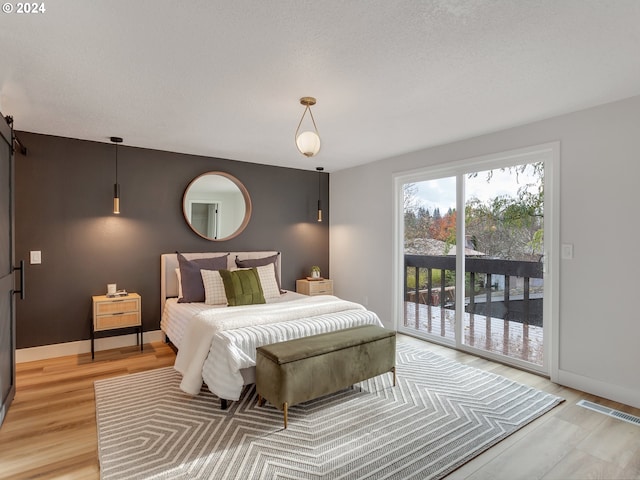 bedroom with light hardwood / wood-style floors, access to outside, and a barn door