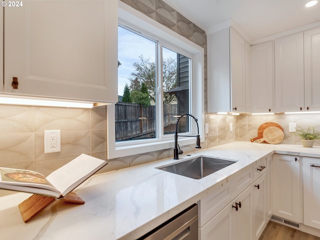 kitchen with backsplash, stainless steel dishwasher, sink, white cabinetry, and light stone counters