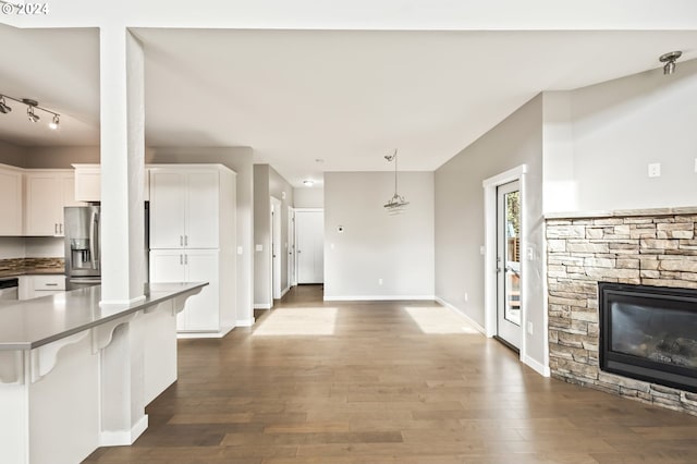 kitchen with hanging light fixtures, white cabinetry, hardwood / wood-style flooring, a stone fireplace, and stainless steel refrigerator with ice dispenser