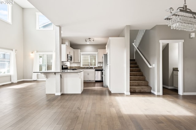 kitchen with appliances with stainless steel finishes, a breakfast bar, white cabinetry, wood-type flooring, and a notable chandelier