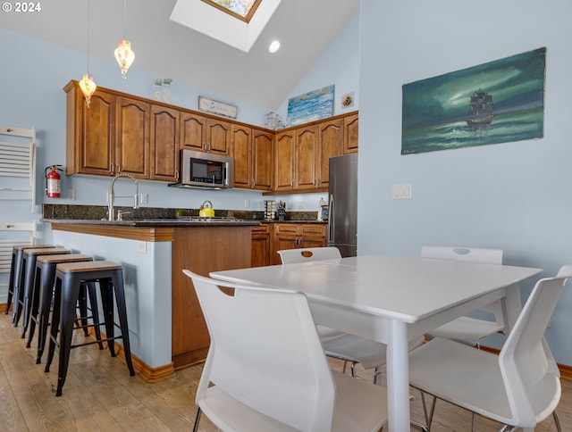 kitchen with stainless steel appliances, a kitchen breakfast bar, high vaulted ceiling, light hardwood / wood-style flooring, and a center island