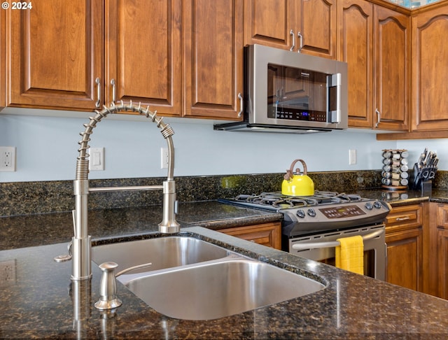 kitchen with stainless steel appliances, dark stone countertops, and sink