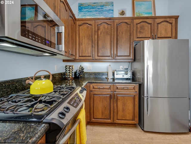 kitchen with stainless steel appliances, dark stone countertops, and light hardwood / wood-style flooring