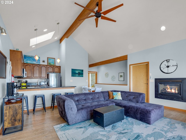 living room with beam ceiling, high vaulted ceiling, light hardwood / wood-style floors, a skylight, and ceiling fan