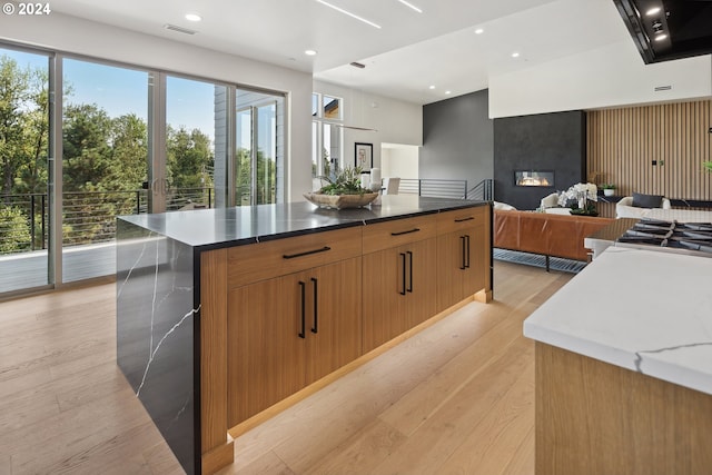 kitchen with a large island, light hardwood / wood-style flooring, dark stone countertops, stainless steel gas stovetop, and a fireplace