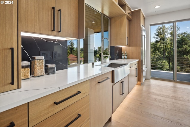 kitchen with light stone counters, light hardwood / wood-style floors, sink, and decorative backsplash