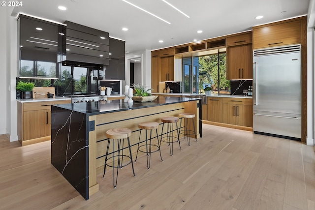 kitchen with a kitchen island, tasteful backsplash, a breakfast bar area, built in refrigerator, and light hardwood / wood-style flooring