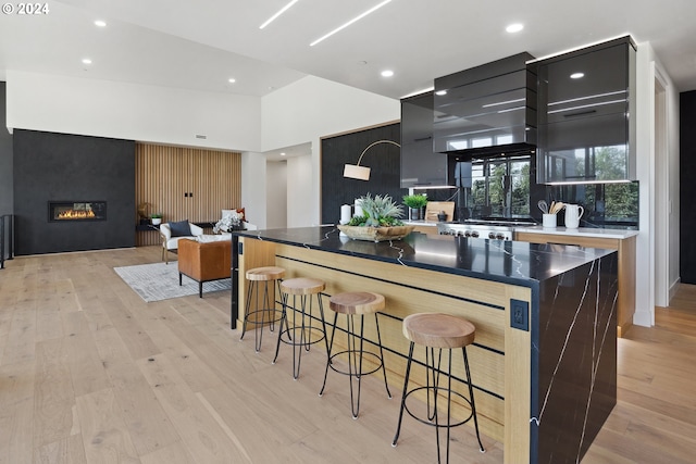 kitchen with a center island, a high ceiling, a kitchen bar, wall chimney exhaust hood, and light wood-type flooring