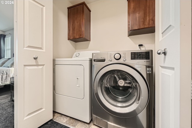 laundry area with washing machine and dryer, light tile patterned floors, and cabinets