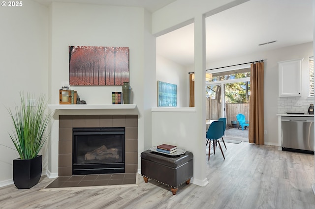 living room featuring a tiled fireplace and light wood-type flooring