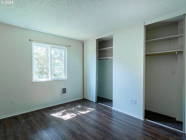 unfurnished bedroom featuring dark hardwood / wood-style flooring, two closets, and a textured ceiling