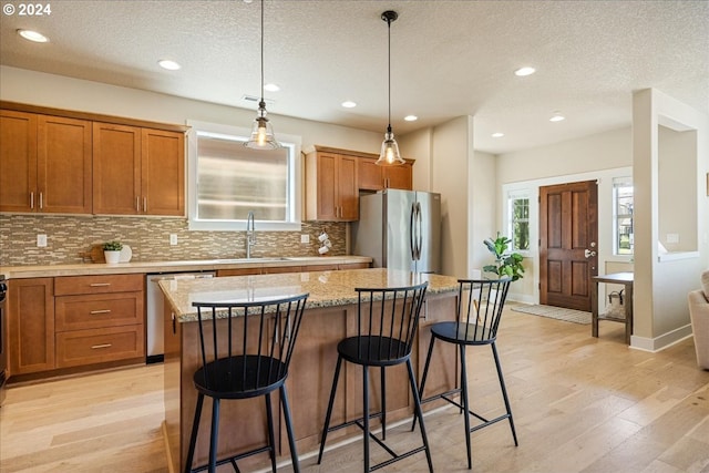 kitchen featuring sink, light hardwood / wood-style flooring, appliances with stainless steel finishes, a kitchen island, and decorative light fixtures