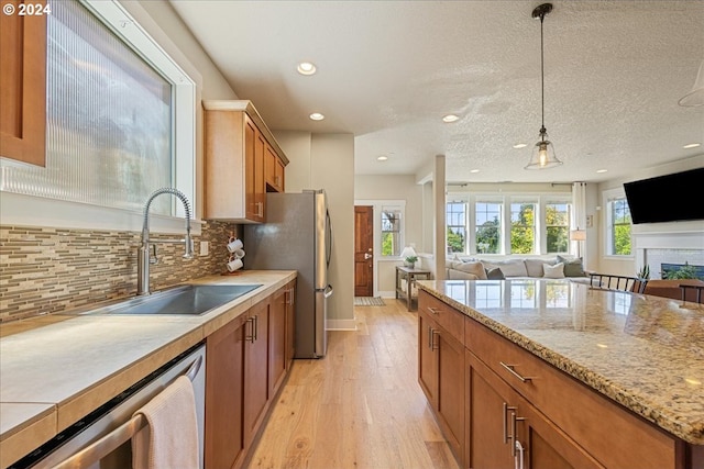 kitchen with sink, appliances with stainless steel finishes, backsplash, hanging light fixtures, and light hardwood / wood-style floors