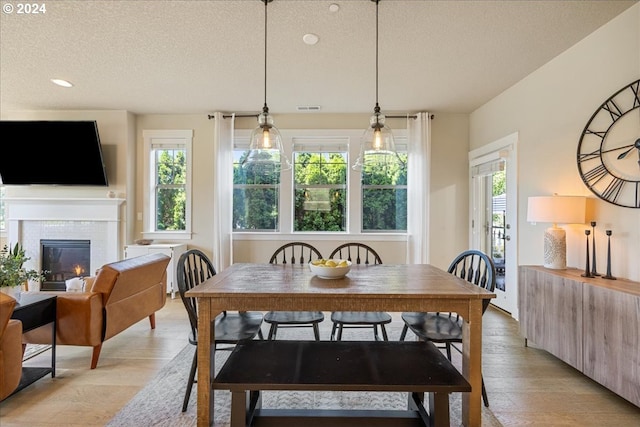 dining room featuring a tiled fireplace, light hardwood / wood-style flooring, and a textured ceiling