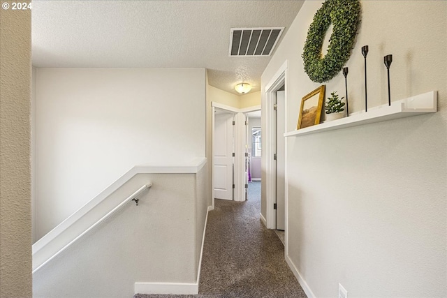 corridor with a textured ceiling and dark carpet