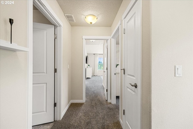 hall with dark carpet and a textured ceiling