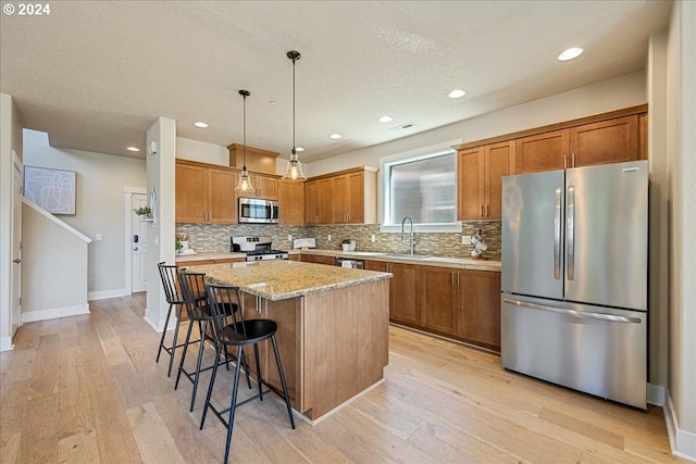 kitchen with sink, appliances with stainless steel finishes, light stone countertops, a kitchen island, and decorative light fixtures