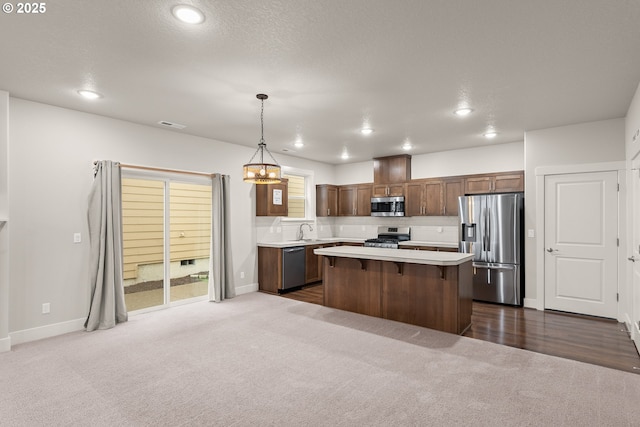 kitchen with a kitchen bar, sink, hanging light fixtures, a kitchen island, and stainless steel appliances