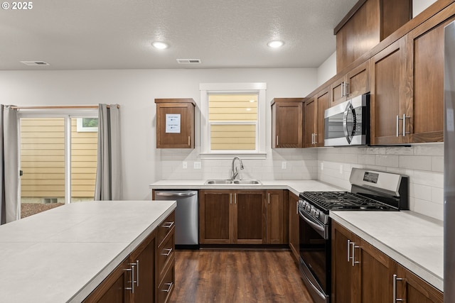 kitchen with appliances with stainless steel finishes, dark hardwood / wood-style floors, sink, backsplash, and a textured ceiling