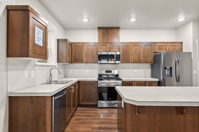 kitchen with appliances with stainless steel finishes, dark hardwood / wood-style floors, a breakfast bar, sink, and backsplash