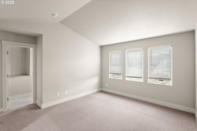 empty room featuring vaulted ceiling, light carpet, and a textured ceiling