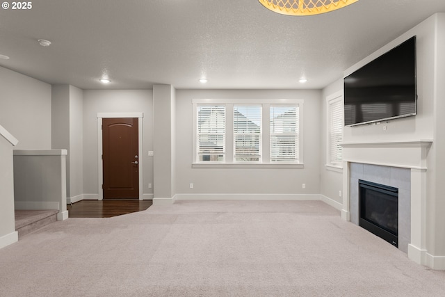 unfurnished living room with light colored carpet, a tile fireplace, and a textured ceiling