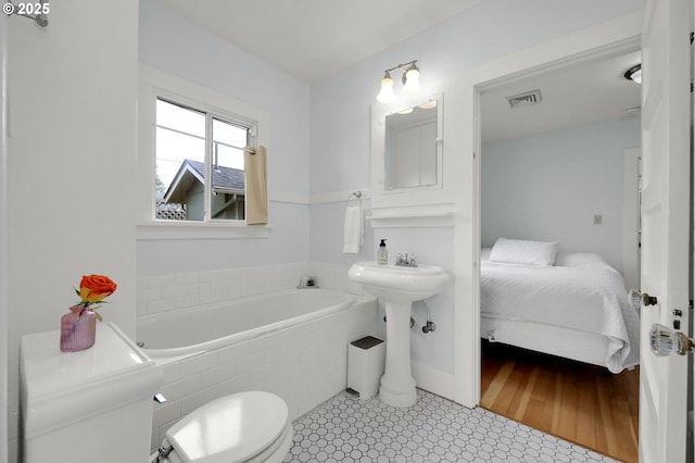 bathroom featuring toilet, tiled bath, and tile patterned floors