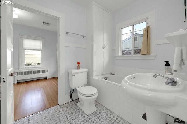 bathroom featuring tile patterned floors, sink, toilet, radiator heating unit, and tiled bath