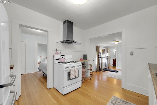 kitchen featuring white cabinetry, light wood-type flooring, wall chimney range hood, and white gas range oven