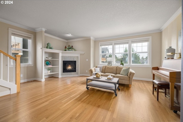 living room featuring a tile fireplace, ornamental molding, light hardwood / wood-style floors, and a textured ceiling