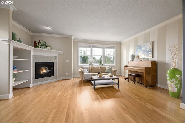 living room featuring light wood-type flooring, a tile fireplace, ornamental molding, and a textured ceiling