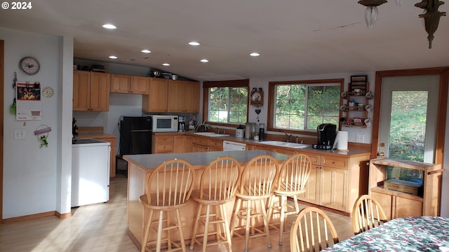 kitchen featuring kitchen peninsula, a kitchen breakfast bar, white appliances, sink, and light hardwood / wood-style flooring