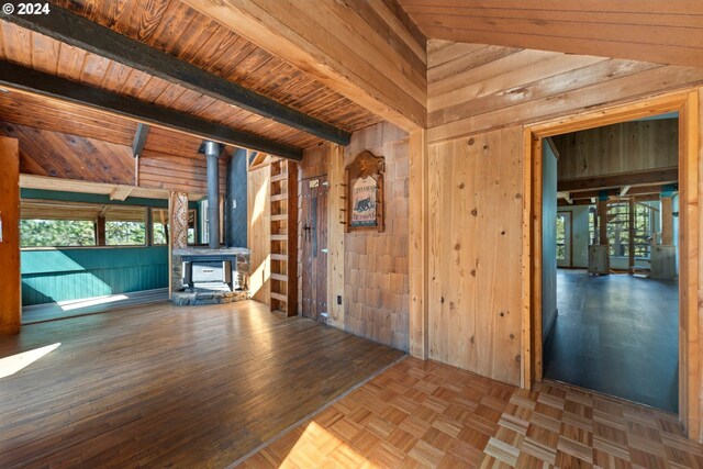 unfurnished living room featuring parquet floors, wood ceiling, wooden walls, a wood stove, and vaulted ceiling