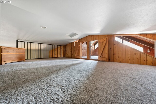 bonus room with carpet flooring, wooden walls, and vaulted ceiling