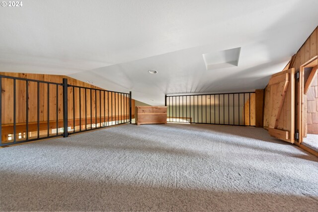 additional living space featuring vaulted ceiling, wood walls, and carpet flooring