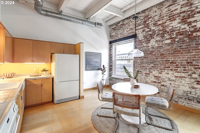 kitchen featuring brick wall, light hardwood / wood-style flooring, tile countertops, a towering ceiling, and white refrigerator