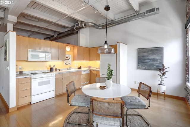 kitchen with white appliances, light brown cabinetry, light hardwood / wood-style floors, hanging light fixtures, and a towering ceiling