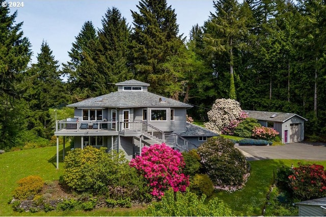 view of front of property featuring a garage, a wooden deck, an outbuilding, and a front yard