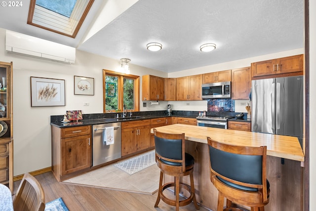 kitchen featuring appliances with stainless steel finishes, a skylight, sink, wooden counters, and a wall unit AC