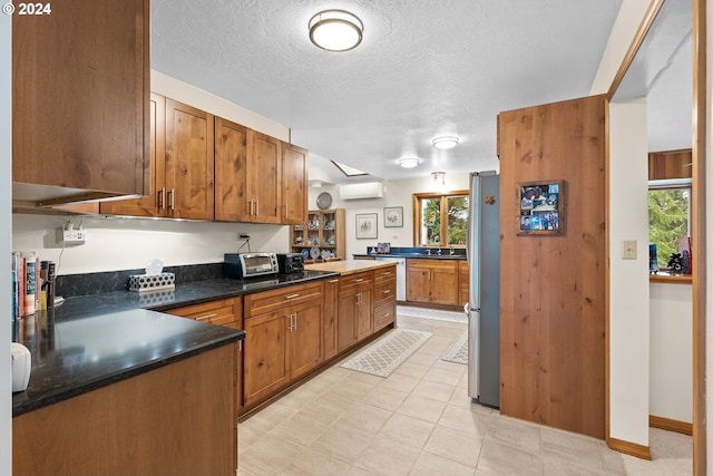 kitchen featuring stainless steel refrigerator, kitchen peninsula, a wall unit AC, and a textured ceiling