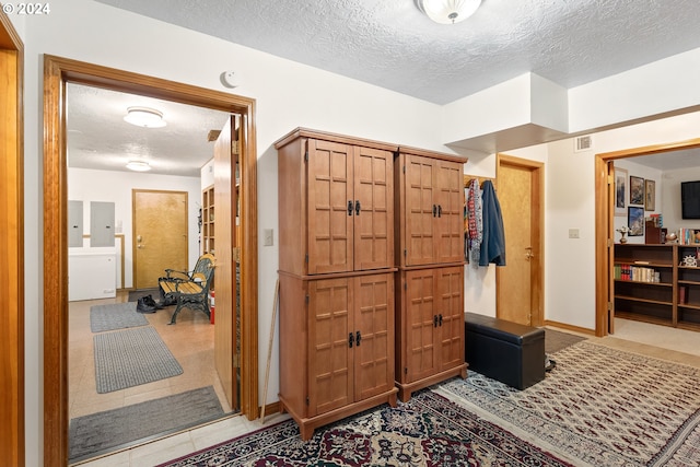 hallway featuring electric panel, a textured ceiling, and light tile patterned flooring