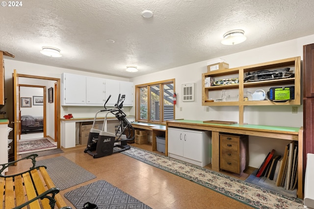 interior space featuring a textured ceiling, built in desk, and white cabinets