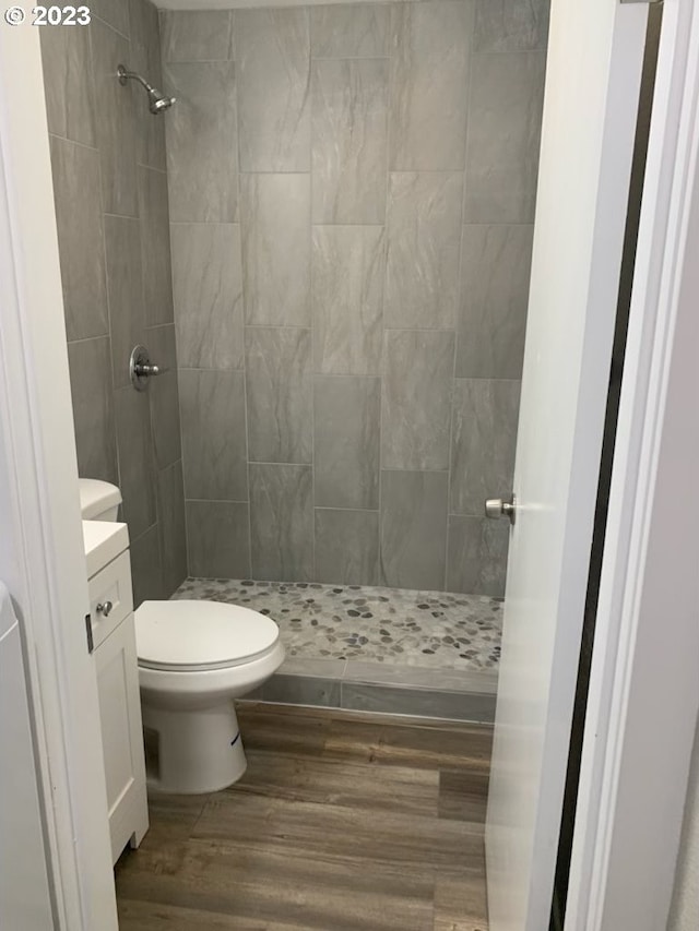 bathroom featuring a tile shower, vanity, toilet, and wood-type flooring