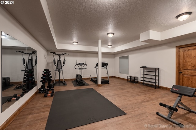 workout room with a raised ceiling, wood-type flooring, and a textured ceiling