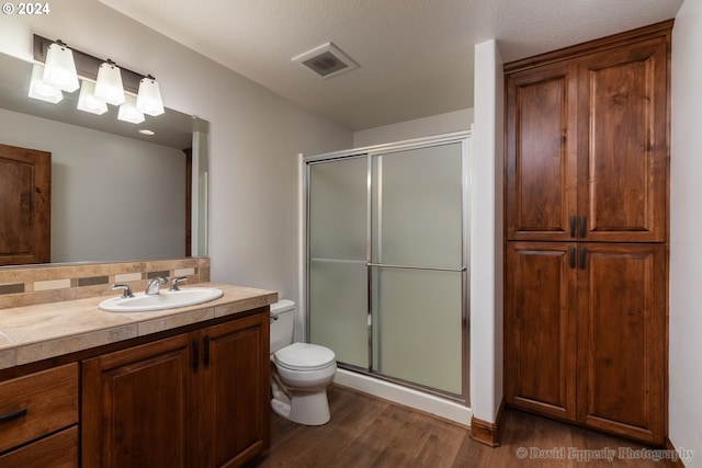 bathroom with vanity, a textured ceiling, hardwood / wood-style flooring, toilet, and a shower with door