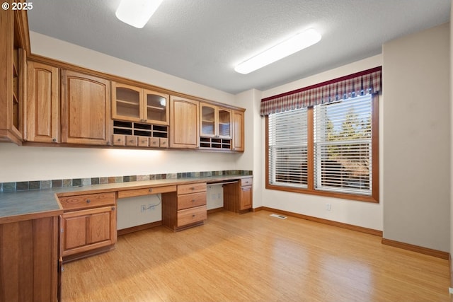 unfurnished office with built in desk, a textured ceiling, and light hardwood / wood-style floors