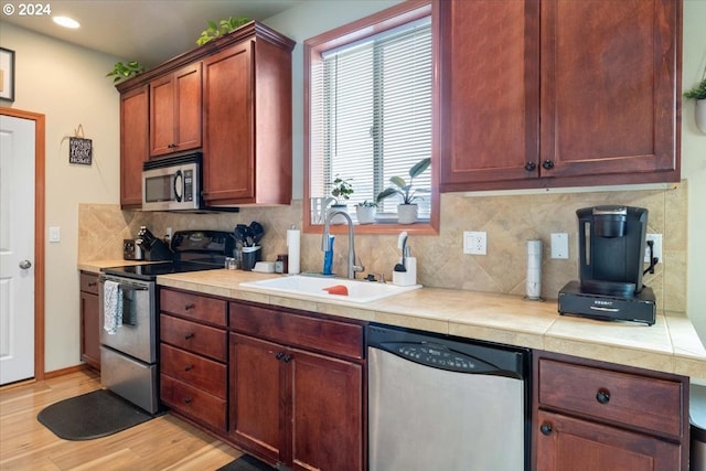 kitchen featuring sink, stainless steel appliances, tasteful backsplash, tile countertops, and light hardwood / wood-style floors