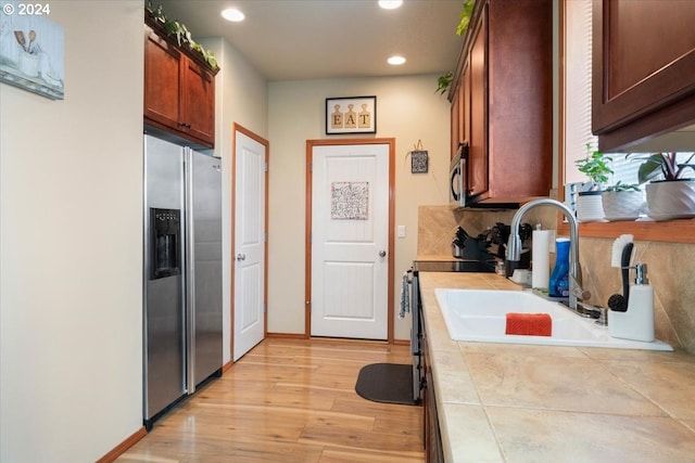 kitchen featuring tile countertops, sink, stainless steel appliances, and light hardwood / wood-style floors