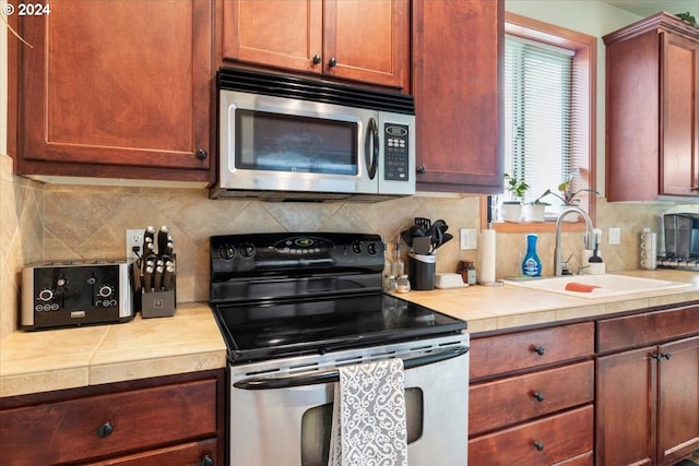 kitchen featuring tile countertops, decorative backsplash, sink, and stainless steel appliances